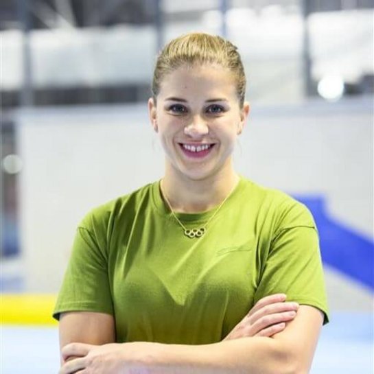 Portrait der Turnerin Elisabeth Seitz in einer Sporthalle, lächelnd in die Kamera blickend, mit grünem T-Shirt und Olympia Kette.