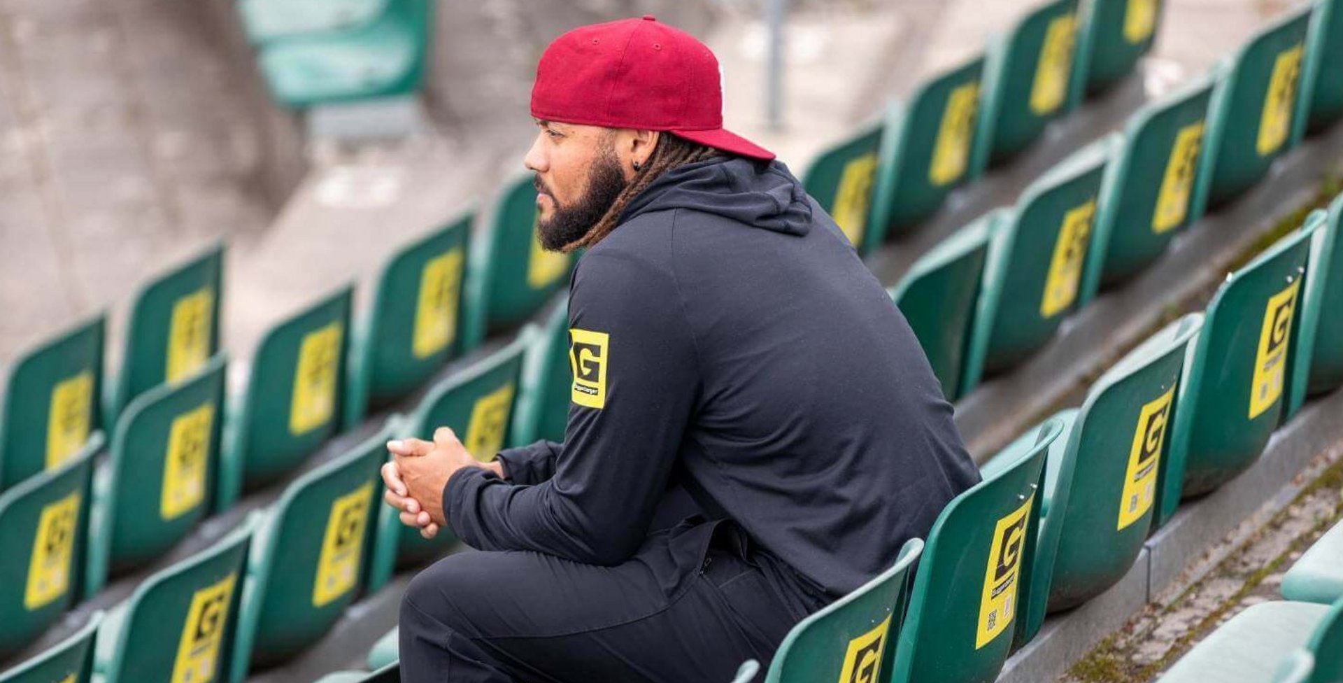 Ein junger Mann sitzt auf einer Tribüne eines Stadions.