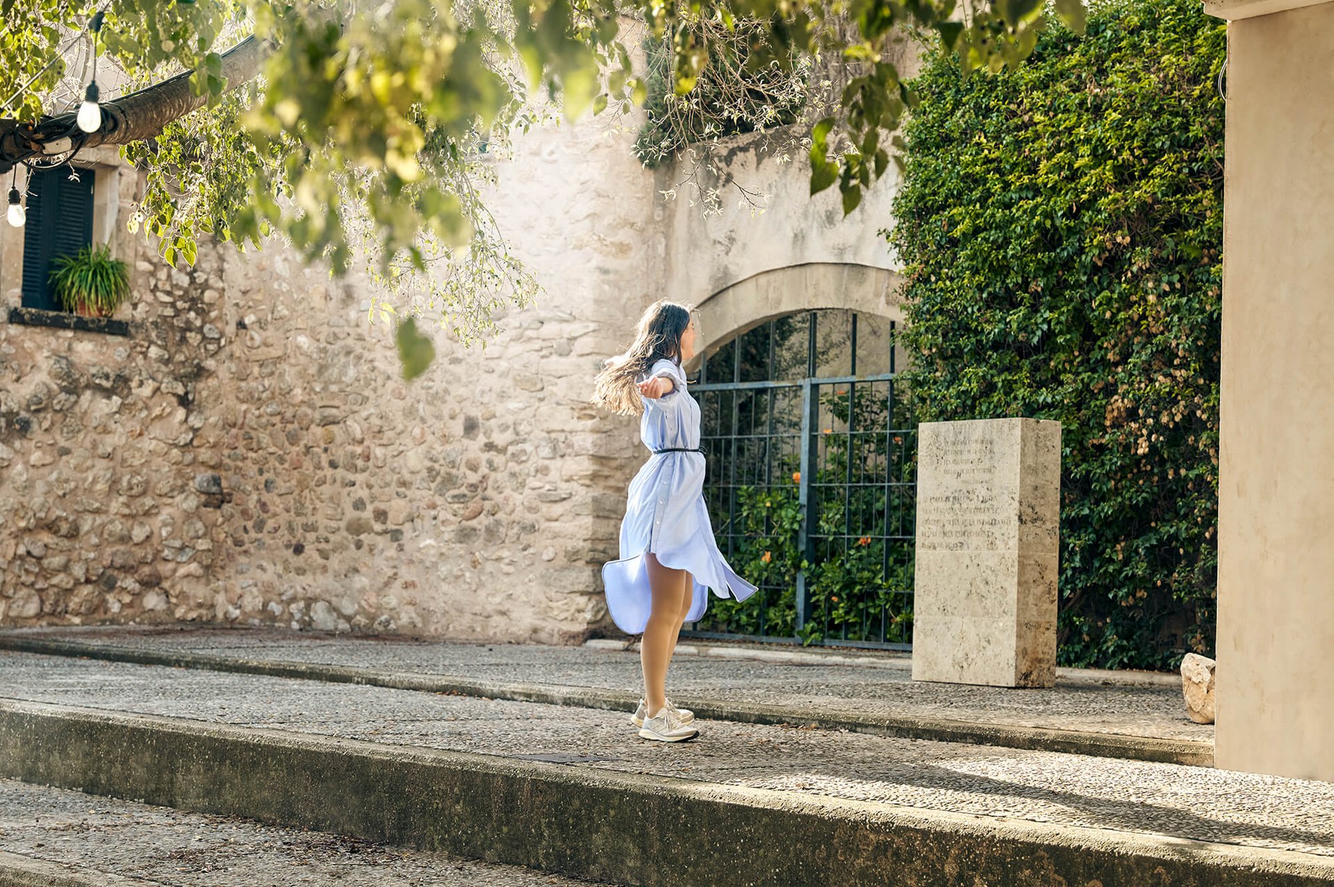 Eine Frau in einem luftigen Kleid tanzt auf einer sonnigen Terrasse, während sie Kompressionsstrümpfe für die Reise trägt, die Komfort und Gesundheit unterwegs fördern.
