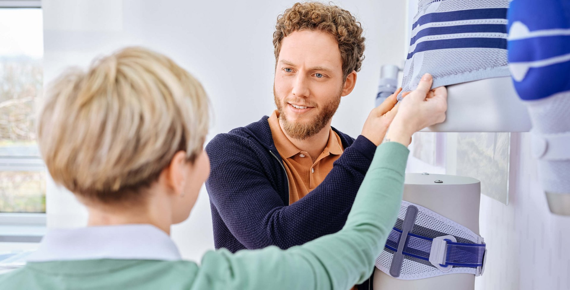 Ein Berater zeigt einer interessierten Patientin die Rückenbandagen von Bauerfeind in einem Showroom.